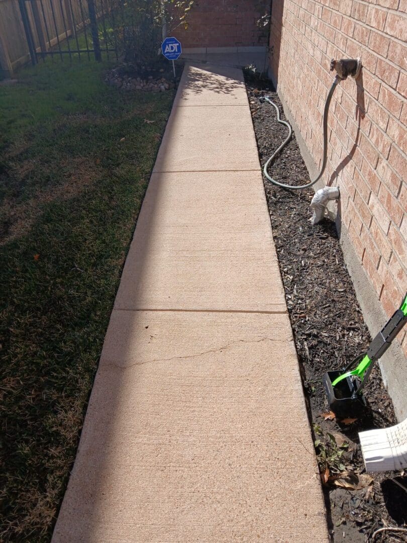 Clean concrete sidewalk next to a brick wall and garden hose.
