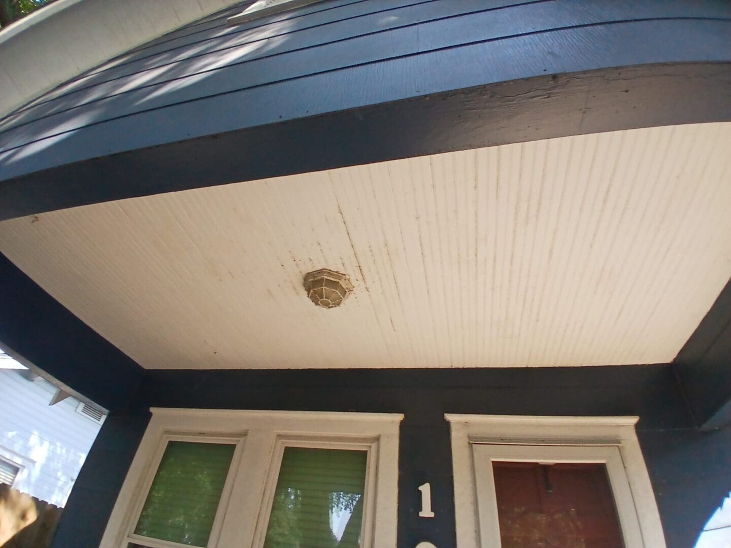 A wasp nest attached to a porch ceiling above a door.