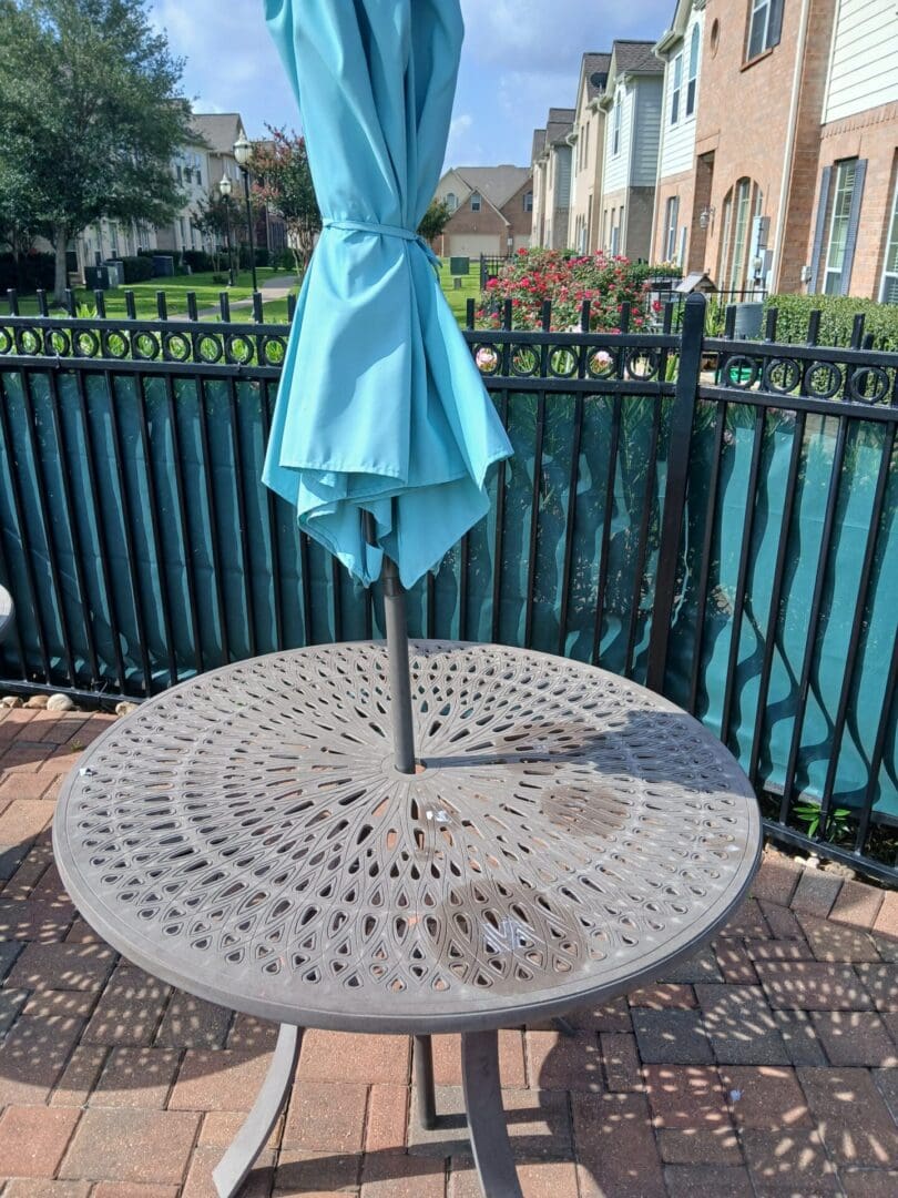 Round metal patio table with closed umbrella in a garden setting.