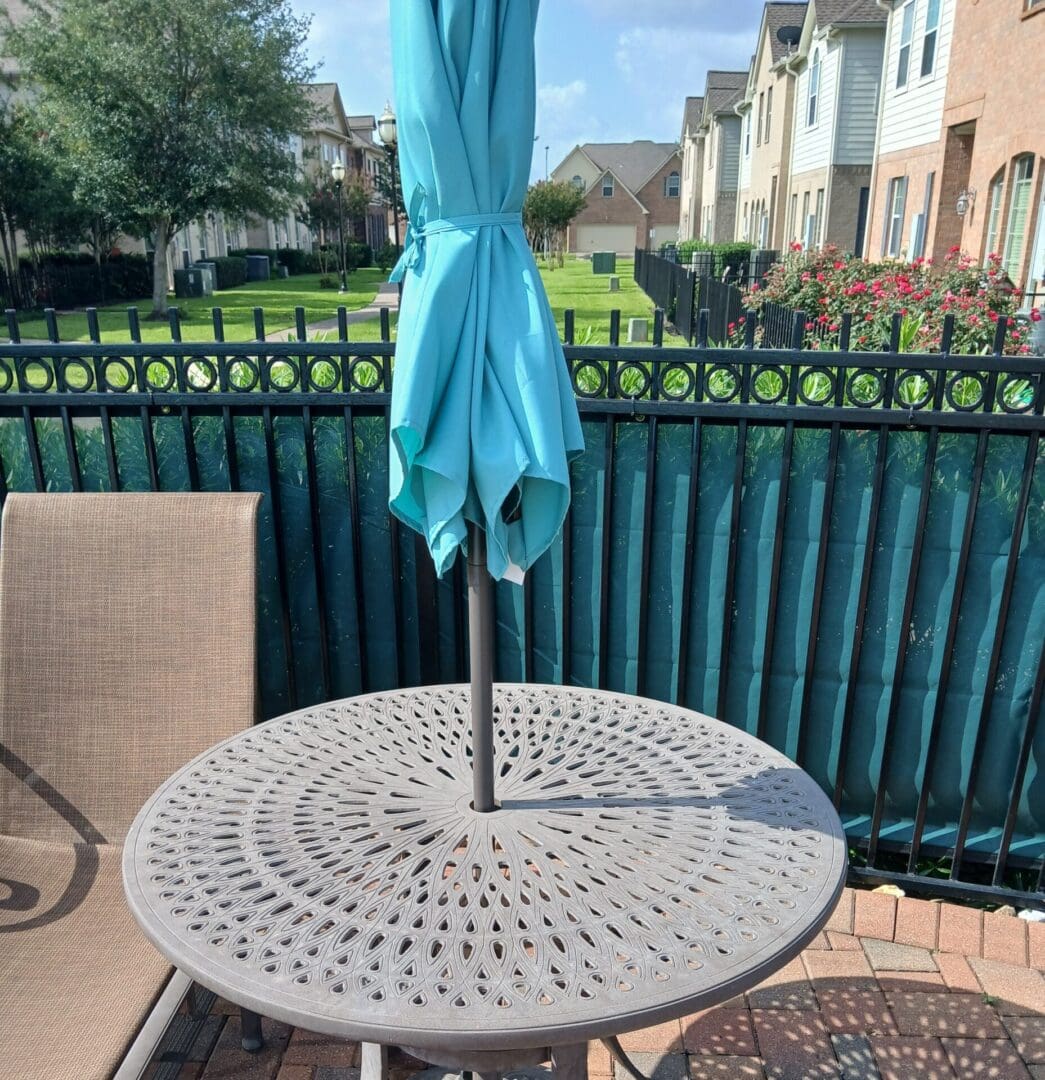 Round outdoor metal table with blue umbrella on a patio.