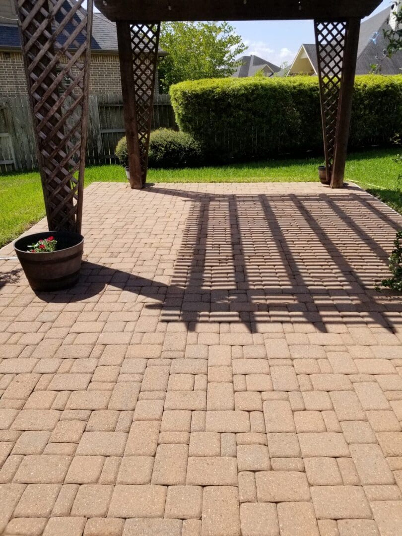 Sunlight casts shadows of a pergola on a brick patio with potted plants.