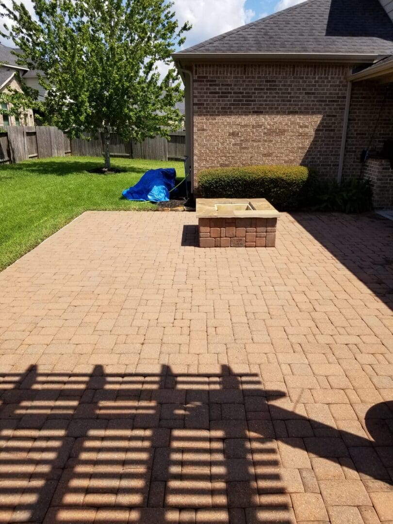 Sunlit brick patio with a small fire pit and green lawn in the background.