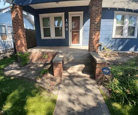 Front porch with steps and brick pillars leading to a doorway.