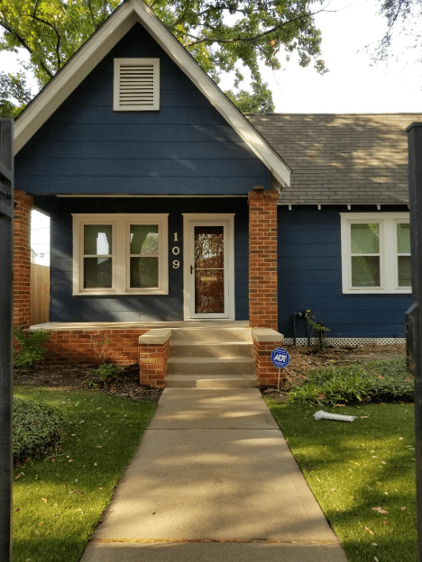 Charming house with brick and blue siding, a welcoming front porch, and a concrete pathway.