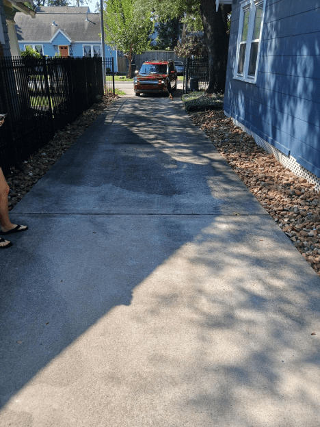 Freshly paved driveway next to a blue building with a truck in the background.
