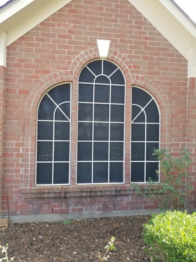 Three arched windows with white grid patterns on a brick wall.