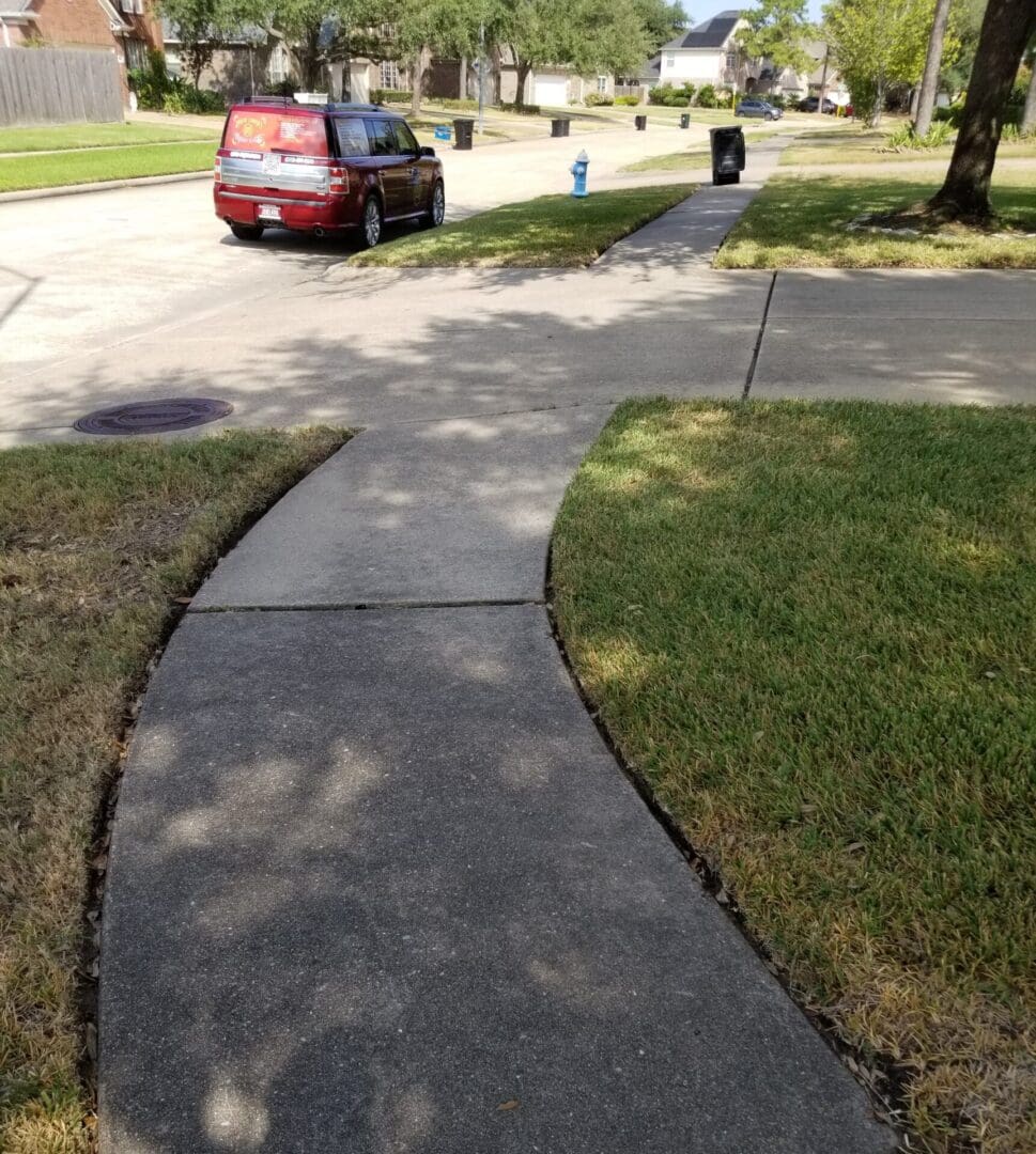 Curved sidewalk bordered by grass and a street with parked cars.