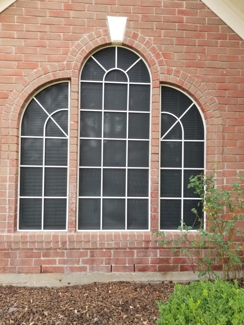 Three arched windows with black grid panes set in a red brick wall.