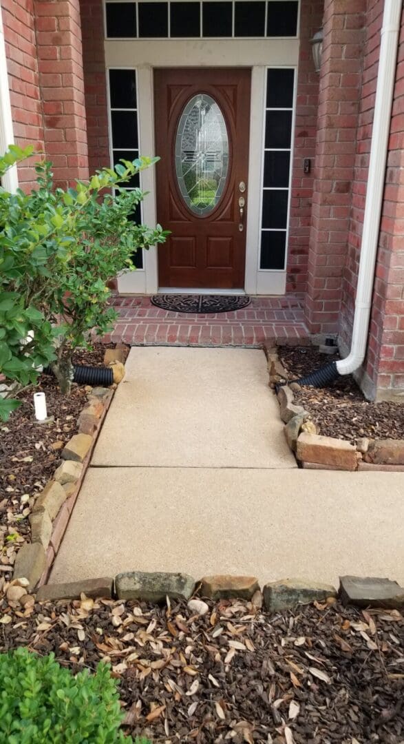 A clean concrete pathway leading to a wooden front door with a small garden on each side.