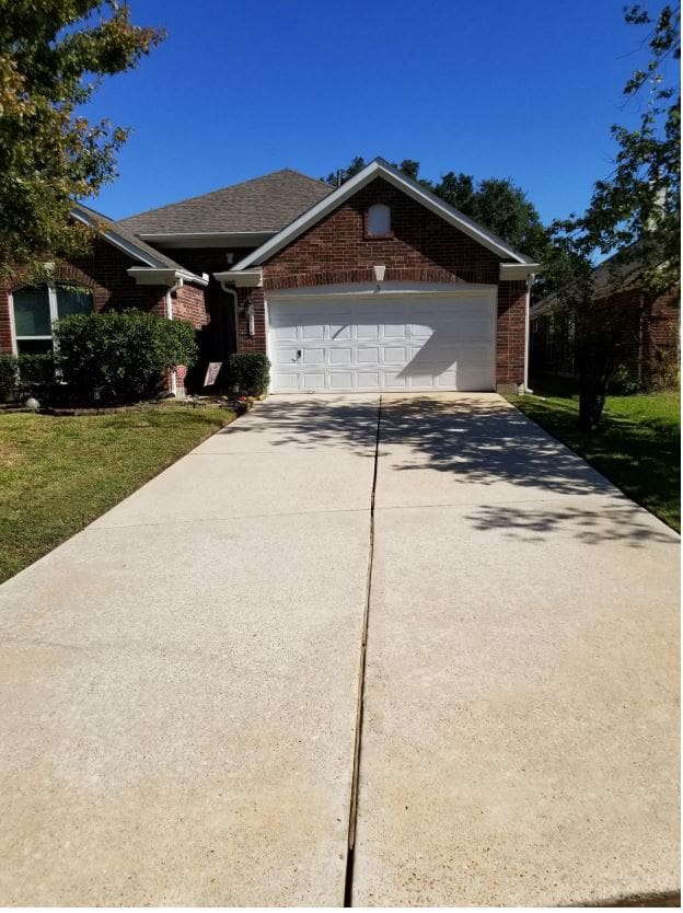 A clean concrete driveway leading to a brick house with a white garage door.